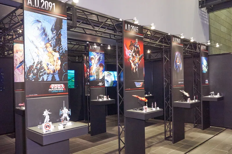 こちらは歴代マクロスシリーズの歴史をテーマにした展示エリア。「HI-METAL R」や「DX超合金」の新規造形も多数含む歴代バルキリーとともに、これも新アイテムの「アクリルスタンドキーホルダー」で歴代の歌姫たち（＆熱気バサラ）が並びました。
「HI-METAL R」では「VF-4 ライトニングIII」「VF-2SS バルキリーII」「VF-0A フェニックス」、「DX超合金」の「YF-19」「VF-19改エクスカリバー 熱気バサラスペシャル」と、参考出品もファン待望の機体揃い。