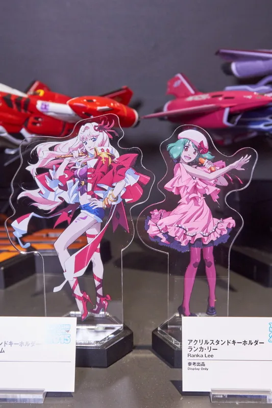 こちらは歴代マクロスシリーズの歴史をテーマにした展示エリア。「HI-METAL R」や「DX超合金」の新規造形も多数含む歴代バルキリーとともに、これも新アイテムの「アクリルスタンドキーホルダー」で歴代の歌姫たち（＆熱気バサラ）が並びました。
「HI-METAL R」では「VF-4 ライトニングIII」「VF-2SS バルキリーII」「VF-0A フェニックス」、「DX超合金」の「YF-19」「VF-19改エクスカリバー 熱気バサラスペシャル」と、参考出品もファン待望の機体揃い。